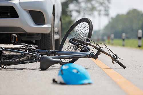 This image shows a bicycle and helmet on the road near a car. If you need a Garden City bicycle accident lawyer, call Cellino Law.